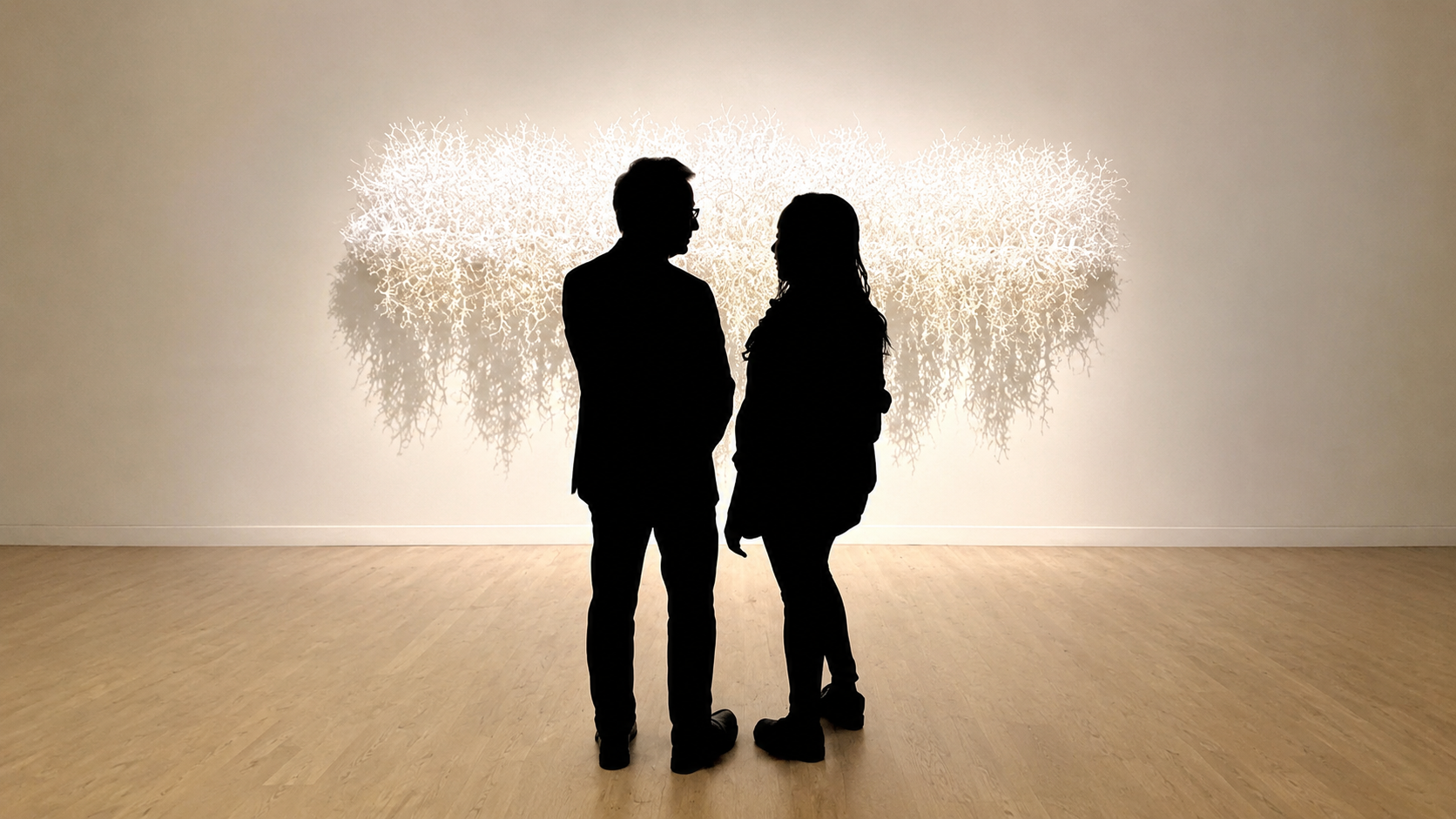 Two black silhouettes facing each other in front of a luminous wall installation.